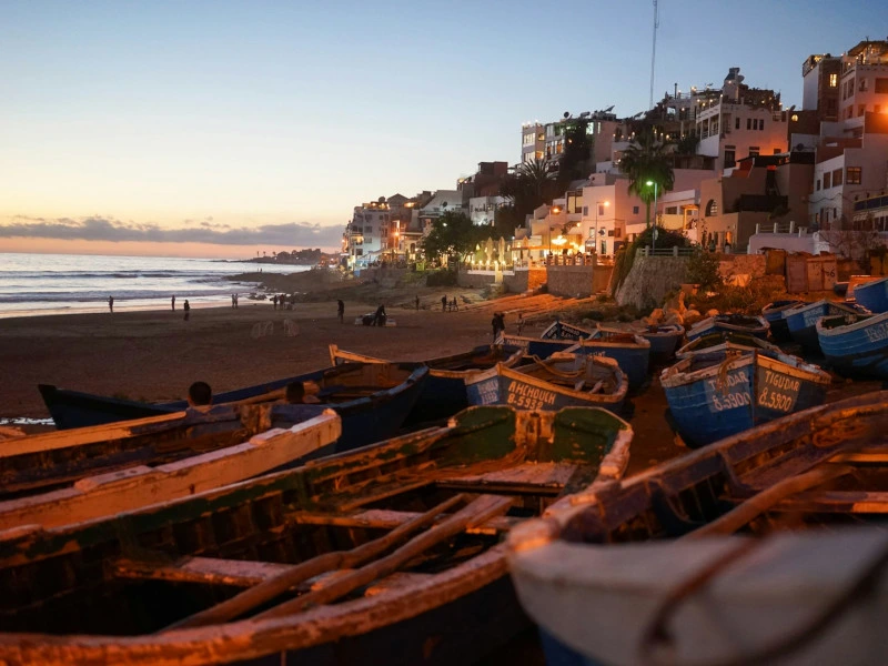 Fischerboote am Strand Afrika bei Sonnenuntergang mit einer Küstenstadt im Hintergrund.