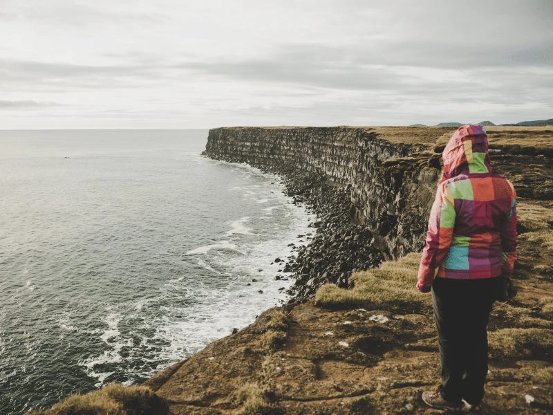 Reisende am Rande steiler Klippen vor der Küste Islands