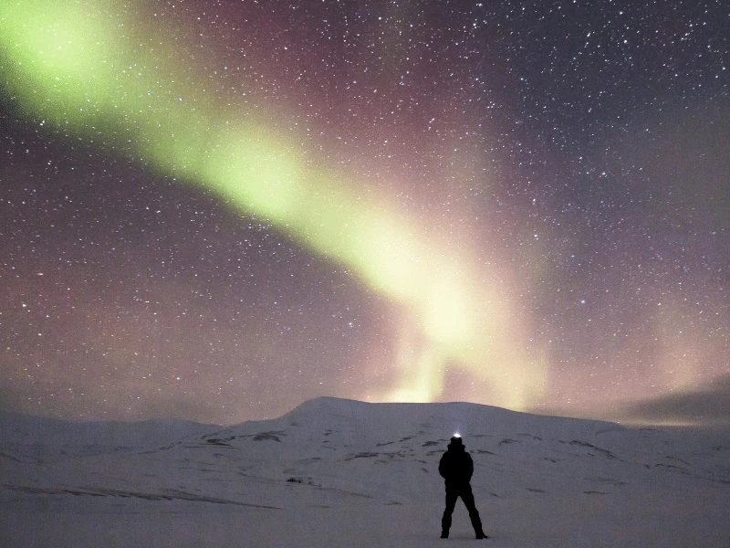 Reisender in einer Schneelandschaft beim Bewundern von Polarlichtern in Island