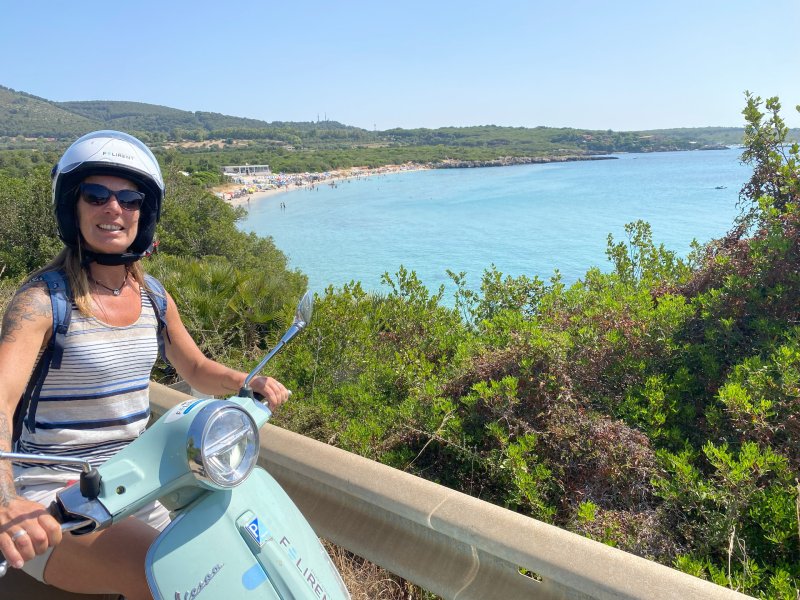 Reisende auf einer Vesper vor blauem Gewässer in Alghero, Italien