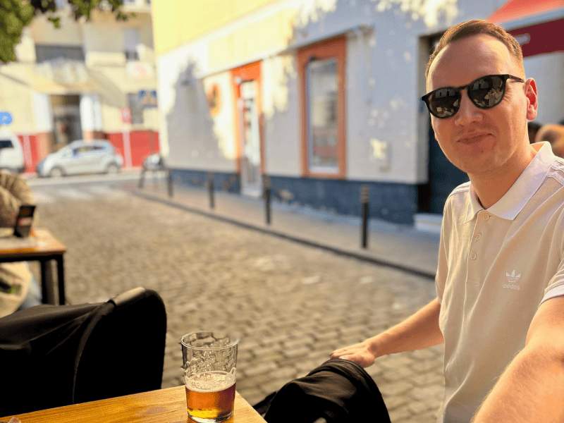 Lächelnder Mann mit Kinderwagen in einer kleinen Gasse an einem Tisch mit einem Getränk