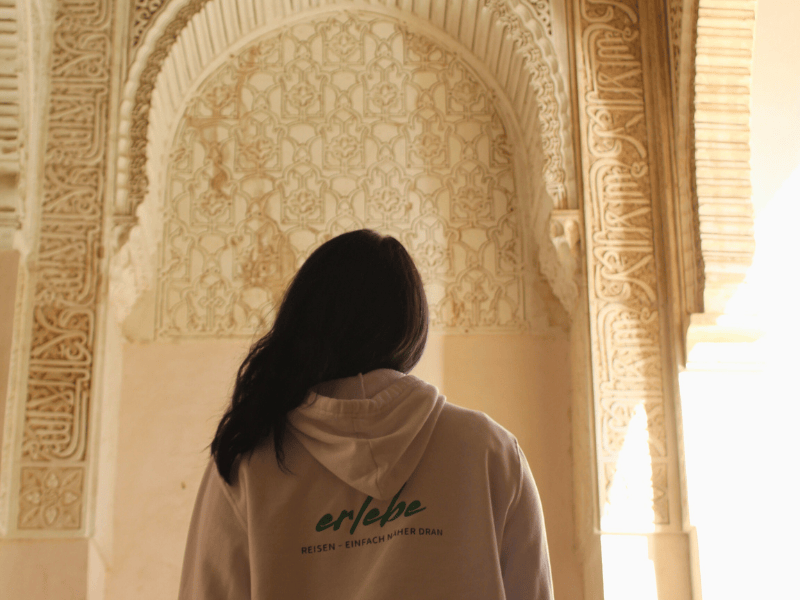 Frau von hinten vor kunstvoll verzierten Wänden der Alhambra