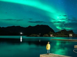 Frau am Wasser stehend unter den Nordlichtern