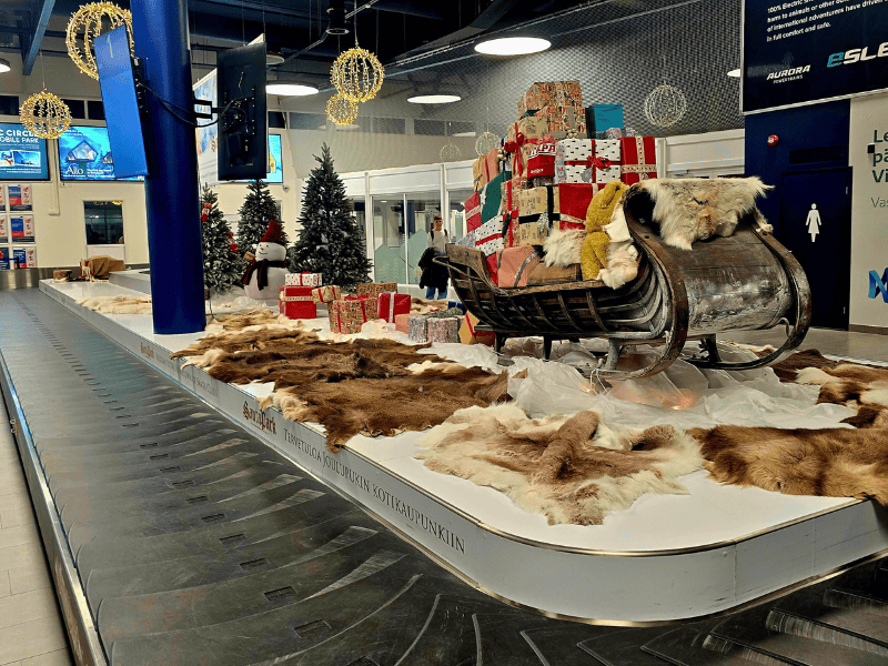 Gepäckausgabeband am Flughafen mit einem Weihnachtsgeschenkeschlitten als Dekoration