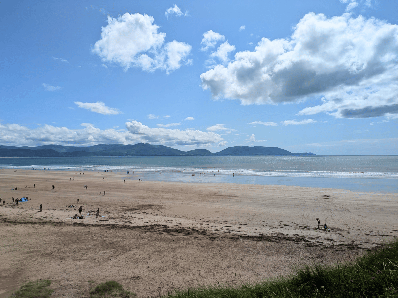 Strand mit wenigen Menschen, dahinter das Meer, Berge und Wolken