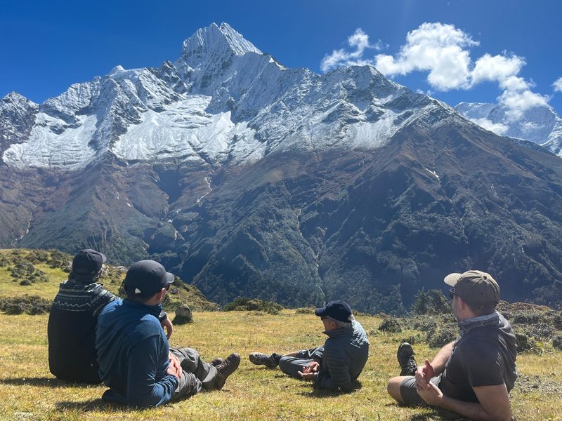 Touristen ruhen sich auf einer Wiese vom Trekking aus und blicken auf das Annapurnagebirge in Nepal