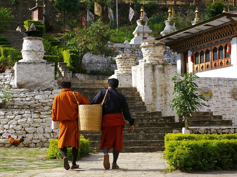 Zwei Einheimische tragen einen Korb zu einem Kloster in Bhutan