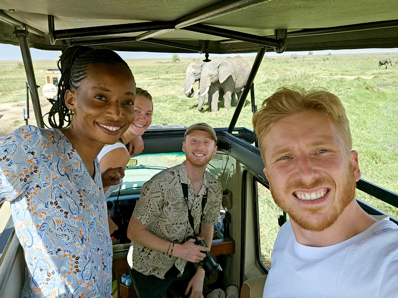 Reisende bei Jeepsafari, im Hintergrund Elefanten