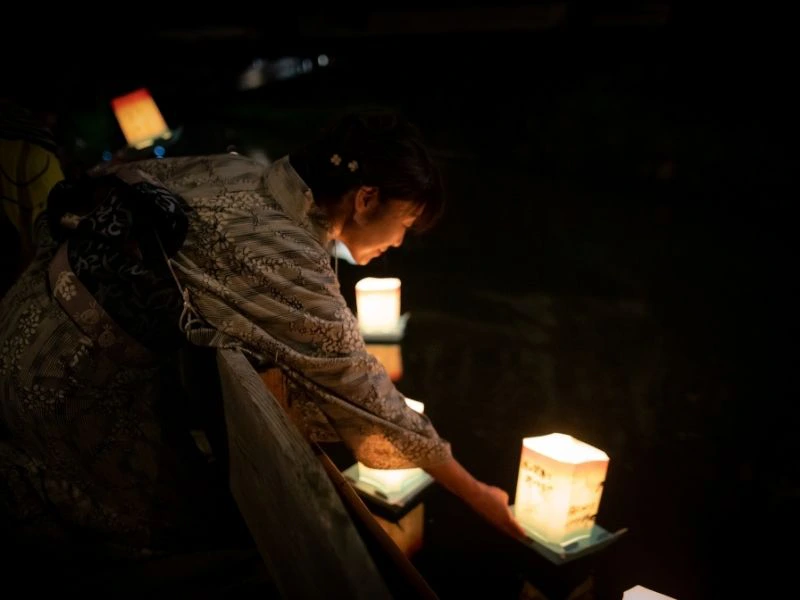Frau legt eine Laterne auf das Wasser zum Obon Fest in Kyoto