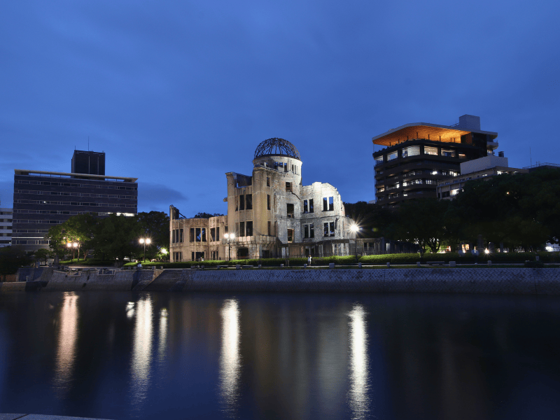 Blick über das Wasser auf das Hiroshima Friedensdenkmal zwischen zwei Gebäuden