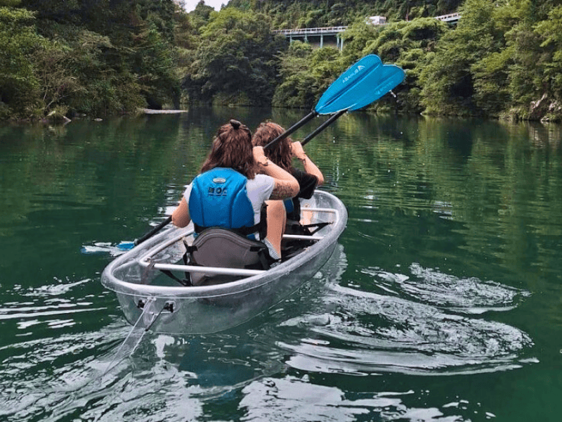 Zwei Reisende von hinten in einem durchsichtigen Kajak auf einem Fluss