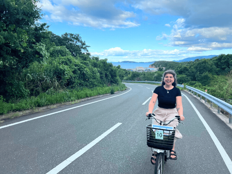 Frau auf dem Fahrrad auf einer StraĂźe ohne Autos, hinter ihr das Meer