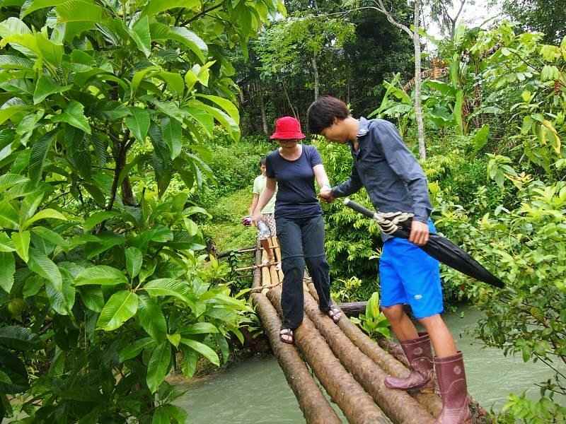 Guide hilft Tourist beim Wandern über eine schmale Brücke in Pu Luong, Vietnam