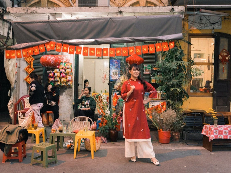 Eine Frau in traditioneller Kleidung steht vor einem mit roten Bannern und Laternen dekorierten Haus