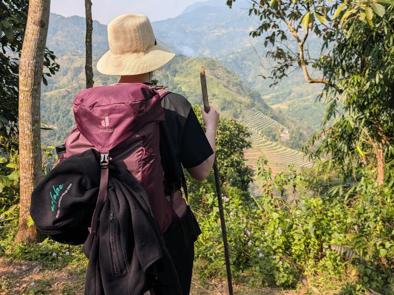 Frau mit Rucksack und Wanderstock blickt aufs Tal hinunter