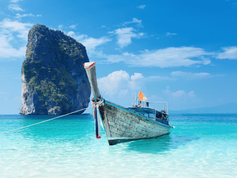 Longtailboot auf klarem Wasser vor einem Kalksteinfelsen in Thailand