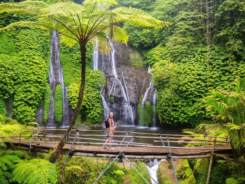 Tourist auf einer Holzbrücke vor einem Wasserfall bei Munduk Bali