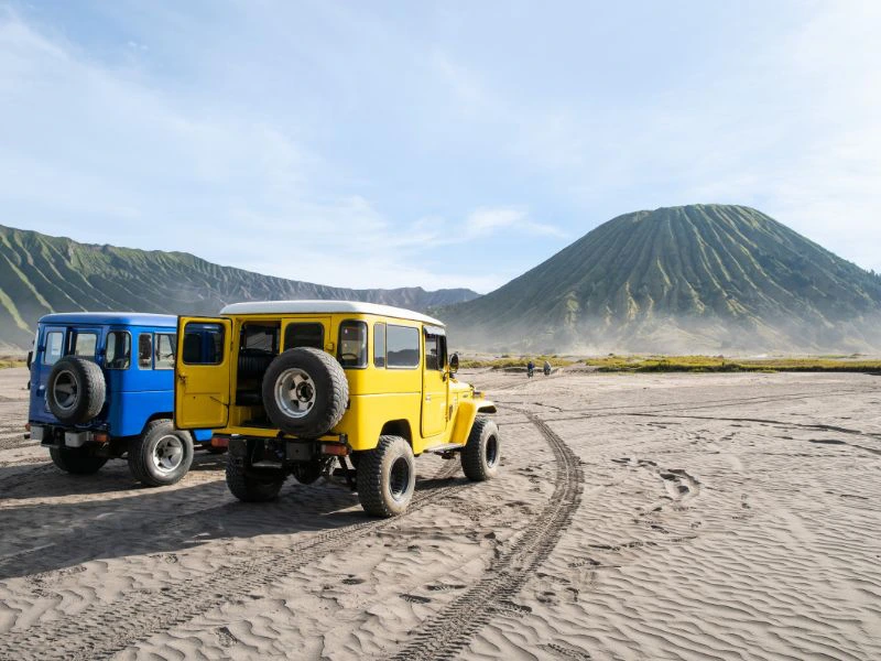 Jeeps parken im Sand vor dem Bromo Vulkan auf Java
