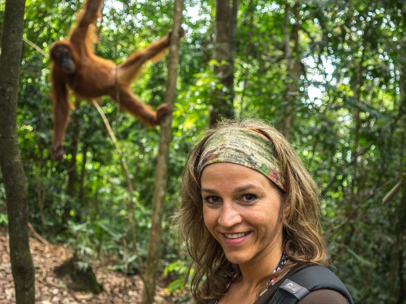 Frau im Dschungel mit einem Orang Utan im Hintergrund in Indonesien