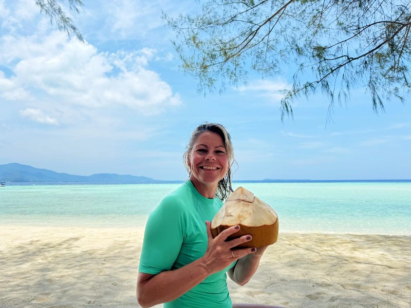 Frau mit Kokosnuss in der Hand am weißen Strand in Indonesien