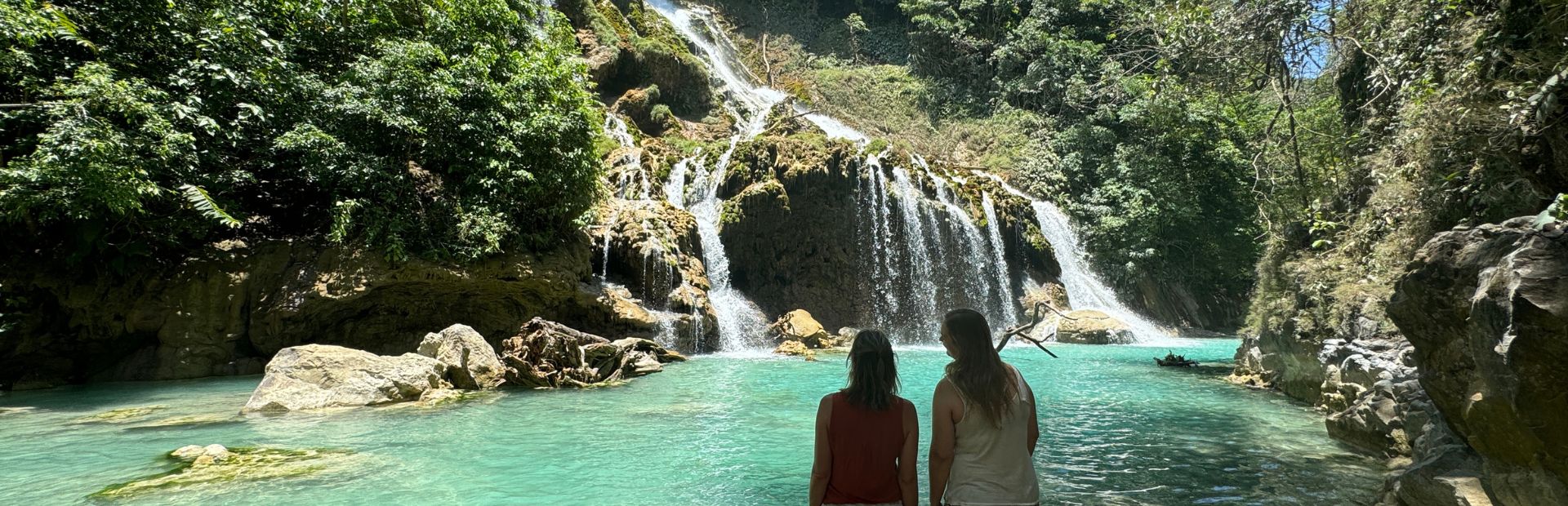 Zwei Reisende vor einem blauen Wasserfall auf Sumba in Indonesien