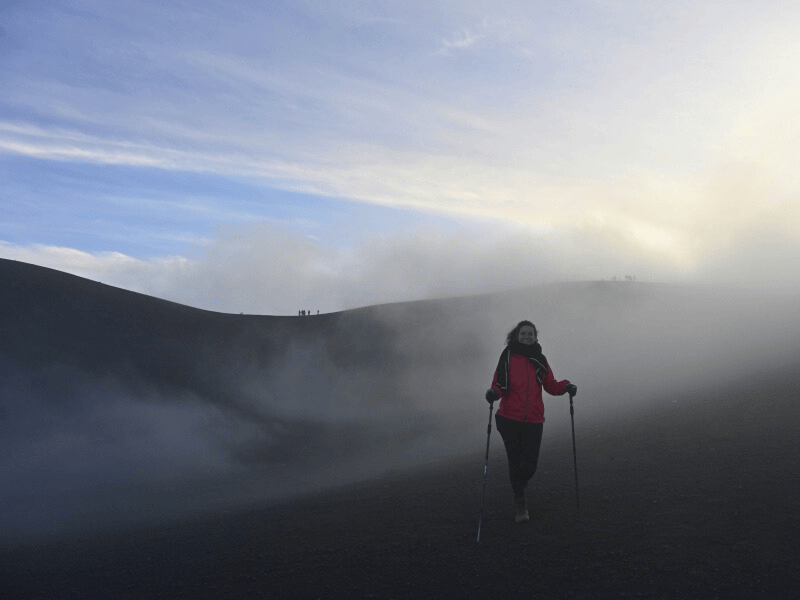 Frau mit Wanderstöcken auf schwarzem Vulkansand bei Sonnenaufgang
