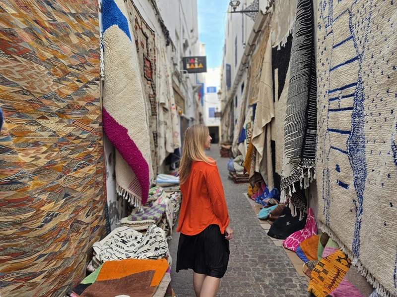 Frau in einer Gasse mit bunten Berberteppichen