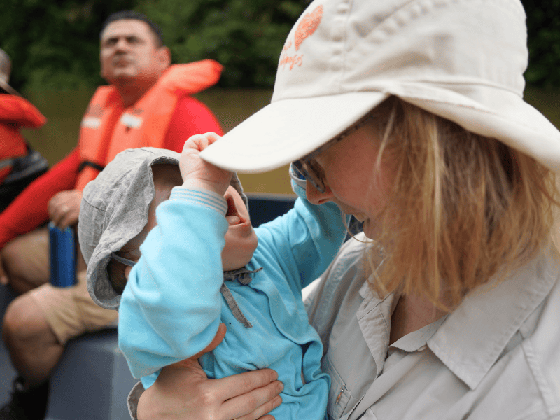 Baby zieht am Hut einer Mutter auf einem Boot