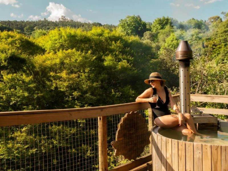 Eine Dame entspannt im Jacuzzi auf der Holzterrasse Ihrer Glamping-Hütte in den grünen Hügeln der Magoebaskloof
