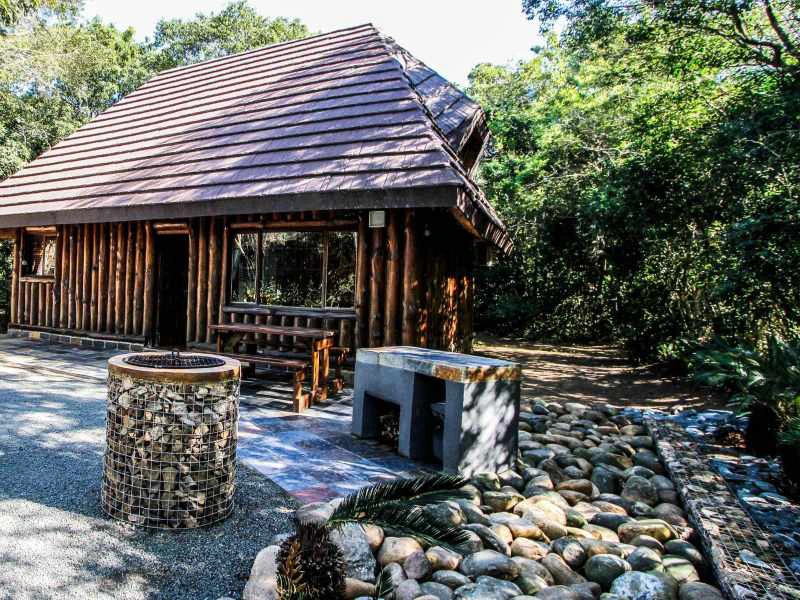 Rustikale Holzhütte mit Steingrill umgeben von Bäumen im Hluhluwe Wildpark