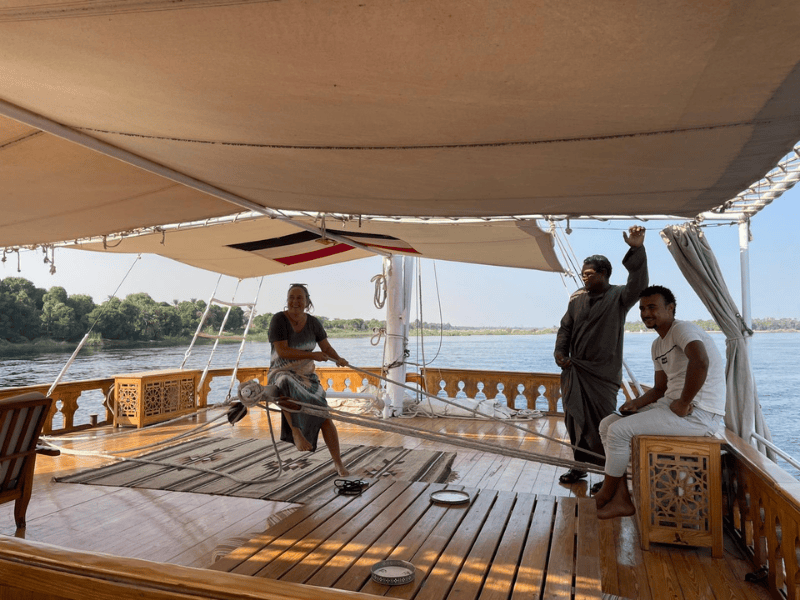 Zwei Crewmitglieder des Bootes schauen zu, wie Touristin an einem Seil zieht