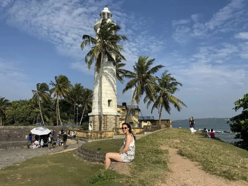 Frau sitzt vor dem Leuchtturm im am Meer in Galle, Sri Lanka