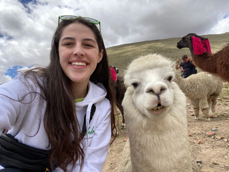 Reisespezialistin Maite mit einem Alpaka in Peru, umgeben von der beeindruckenden Landschaft der Anden