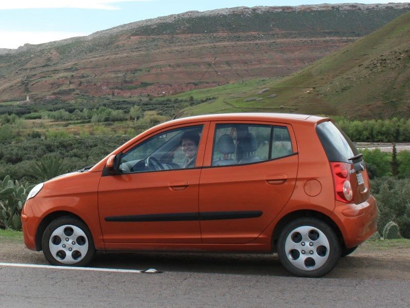 Kleiner orangener Mietwagen vor einem Berg