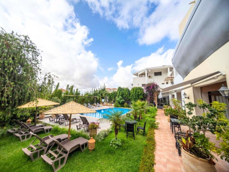 Hotel mit Pool, Liegestühlen und grünem Garten in Tanger in Marokko unter blauem Himmel mit Wolken.