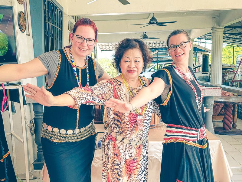 Touristinnen und eine Einheimische in traditionellen Gewändern auf Borneo