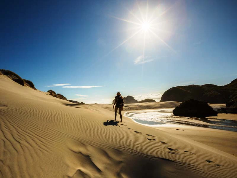 Person spaziert bei strahlendem Sonnenschein über den Strand in der Golden Bay in Neuseeland.