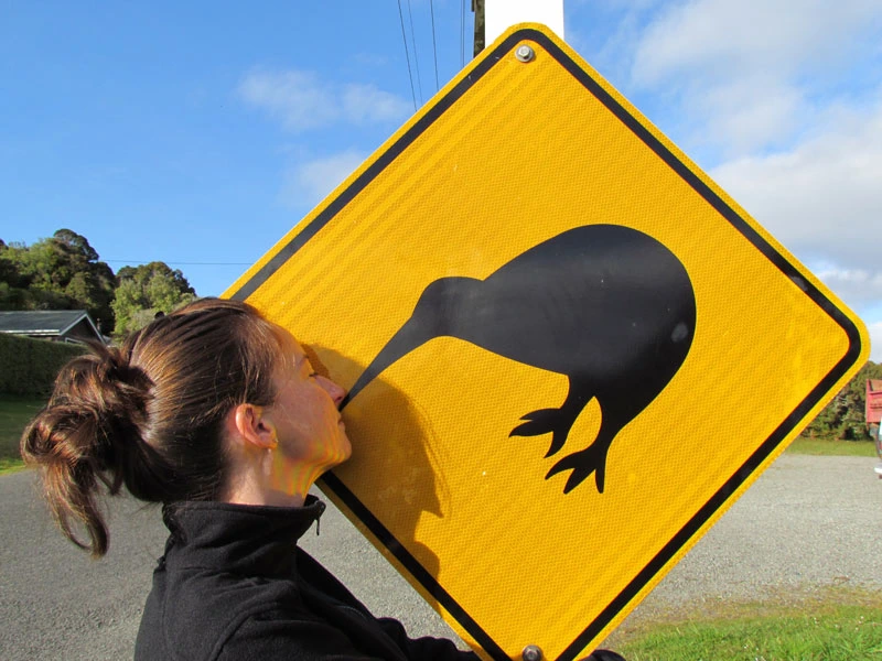 Frau küsst die Abbildung eines Kiwis auf einem gelben Schild auf Stewart Island in Neuseeland.