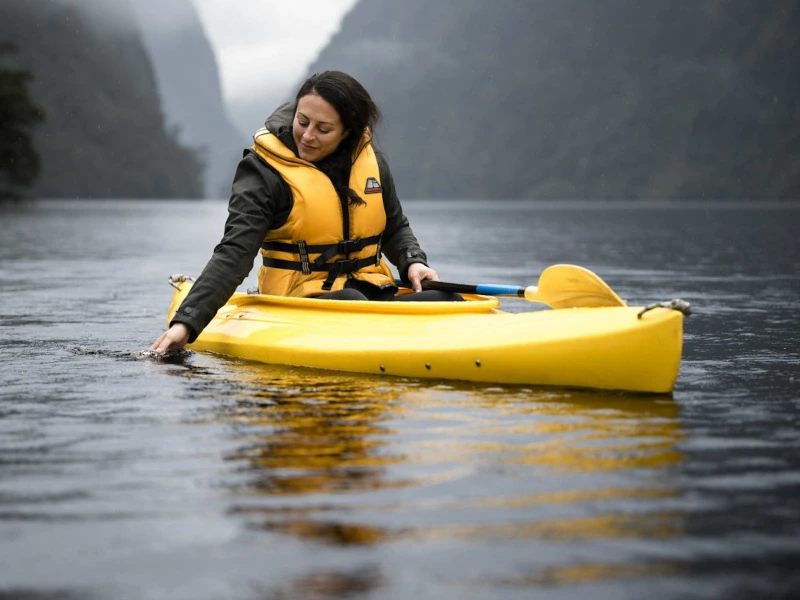 Frau mit Schwimmweste sitzt im gelben Kajak im Doubtful Sound in Neuseeland.