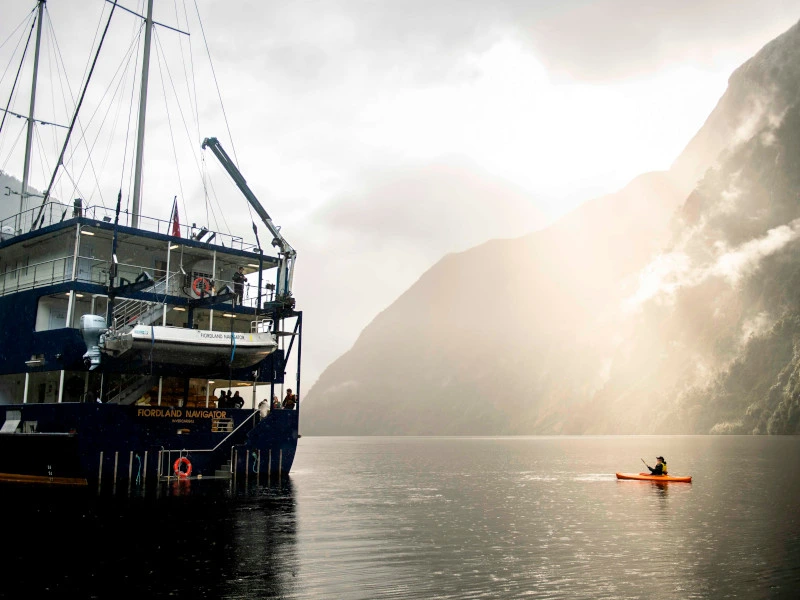 Kajak fährt neben einem großen Schiff im Doubtful Sound in Neuseeland.