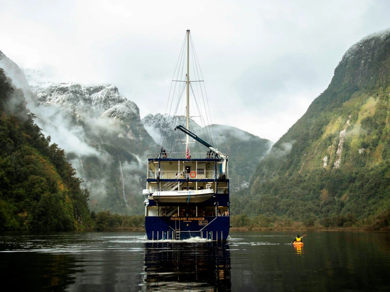 Kajak fährt neben einem großen Schiff im Doubtful Sound in Neuseeland.