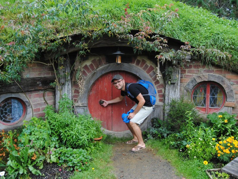 Mann posiert vor einem kleinen Höhleneingang in Hobbiton, Neuseeland