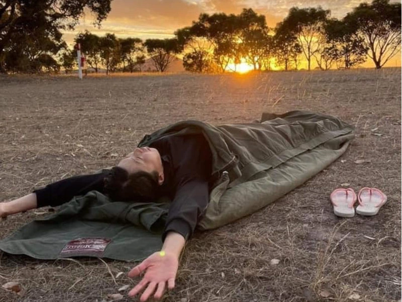 Person liegt bei Sonnenaufgang im Swag im Outback in Australien