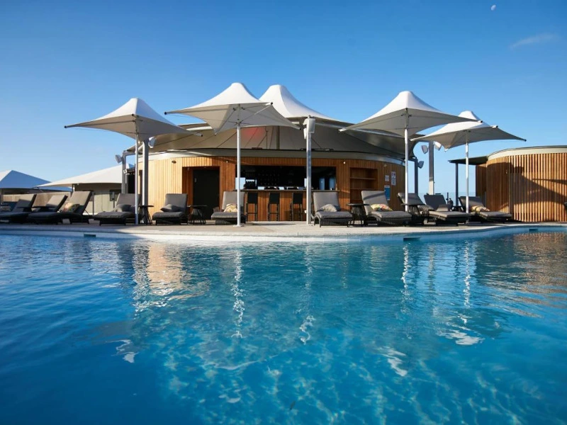 Liegestühle unter Sonnenschirmen stehen zwischen Pool und Pool-Bar auf Rottnest Island in Australien.