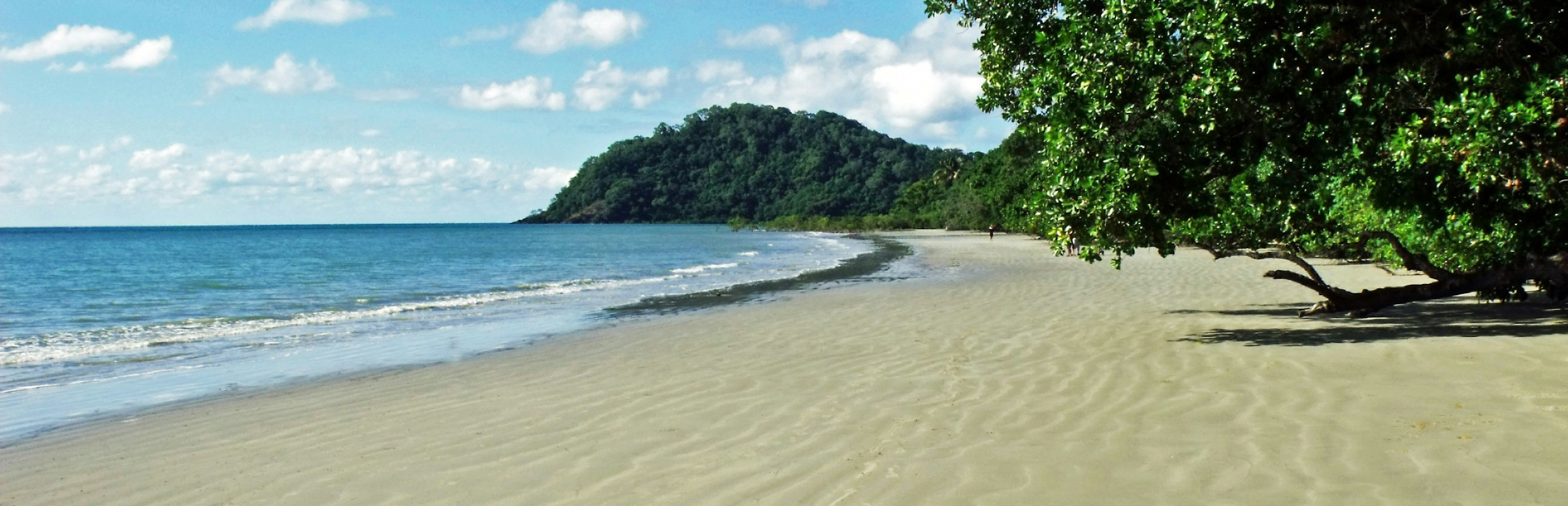 Australischer Strand mit weißen Sand, blauen Himmel und etwas grüne Natur