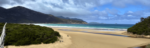 Strand mit Fluss, der ins Meer mündet, im Hintergrund Berge
