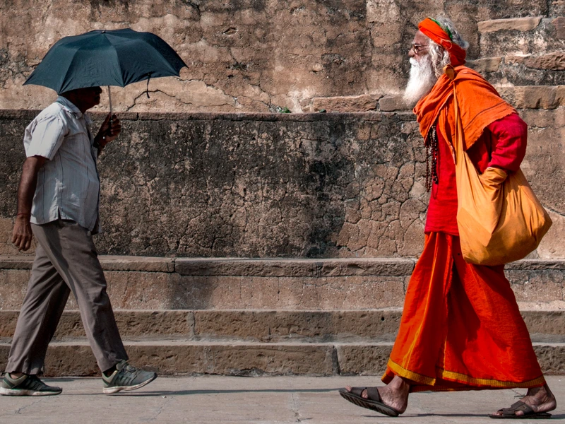 Alter Hindumönch im orangenen Gewand und ein Bürger Mumbais mit einem Sonnenschirm