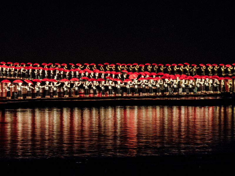 Steg voller Darsteller mit Schirmen bei der Lichtershow in Yangshuo in China