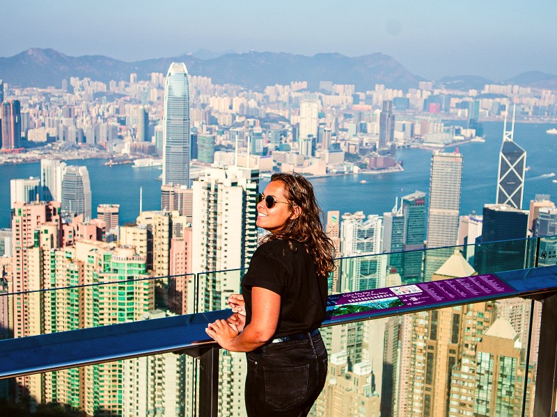 Frau blickt von einer Aussichtsplattform über die Skyline von Hong Kong