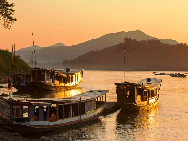 Boote bei Sonnenuntergang am Ufer des Mekongs in Laos